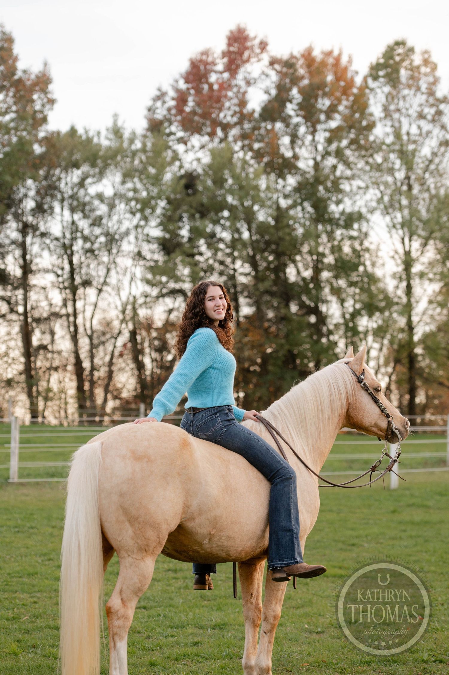 Equestrian portrait featuring rider on palomino horse against autumn trees.