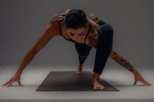 A person performs a deep yoga stretch on a dark mat against a gray background, demonstrating flexibility and strength.
