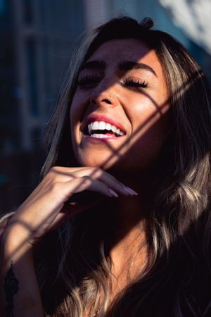 Portrait of someone laughing with bright white teeth and dark hair backlit by sunlight casting dramatic shadows.