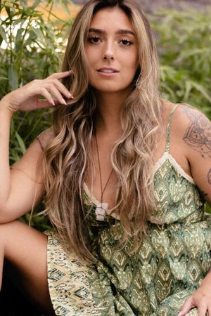 Outdoor portrait with long wavy blonde hair wearing green patterned dress and crystal necklace in natural setting.