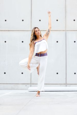 A graceful dancer in white clothing strikes an elegant pose against a modern concrete wall with circular accents.