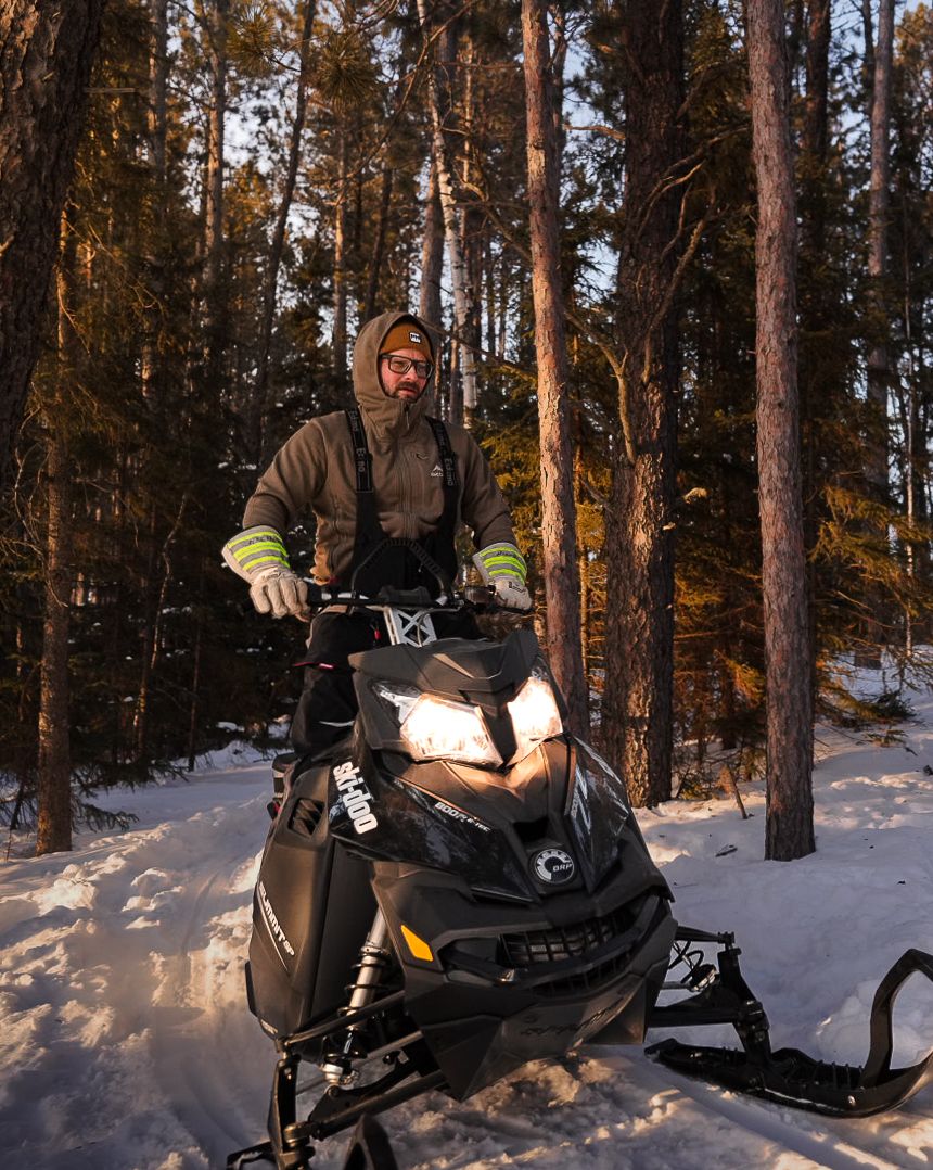 Snowmobile rider enjoying winter trails through snow-covered pine forest at sunset.