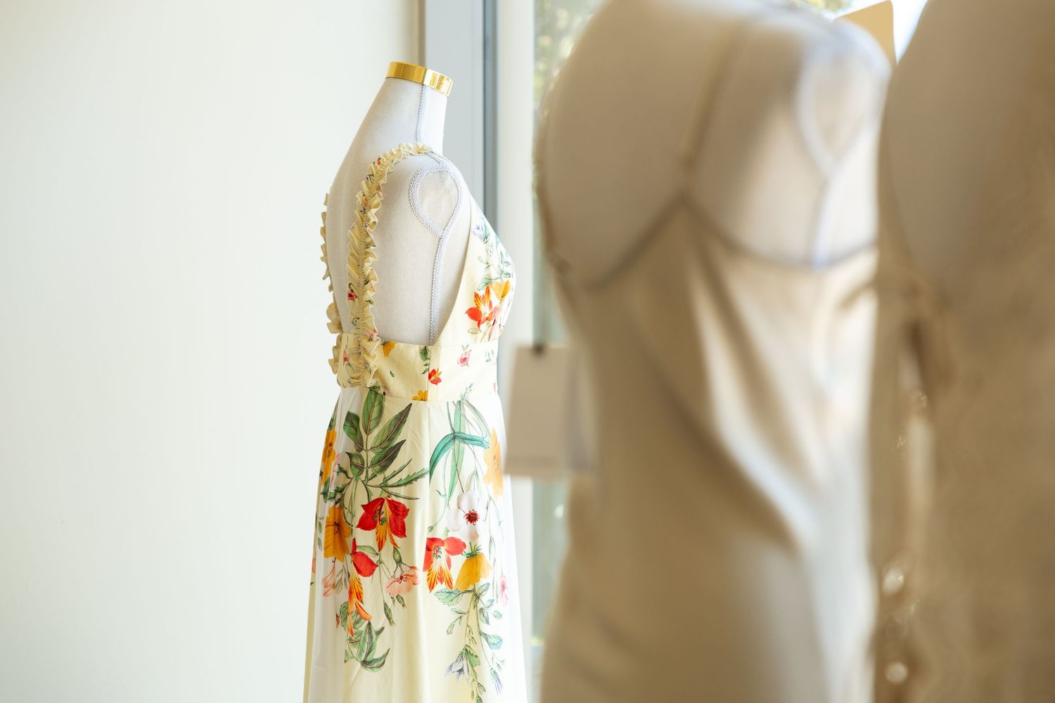 Floral white dress and solid dress hanging near window with soft lighting.