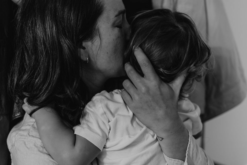 b&w photo of a mom kissing the oldest son after coming back from the hospital where she gave birth, missing him very much