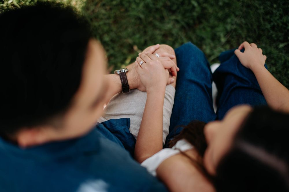 Close-up view of couple holding hands while sitting in a park setting.