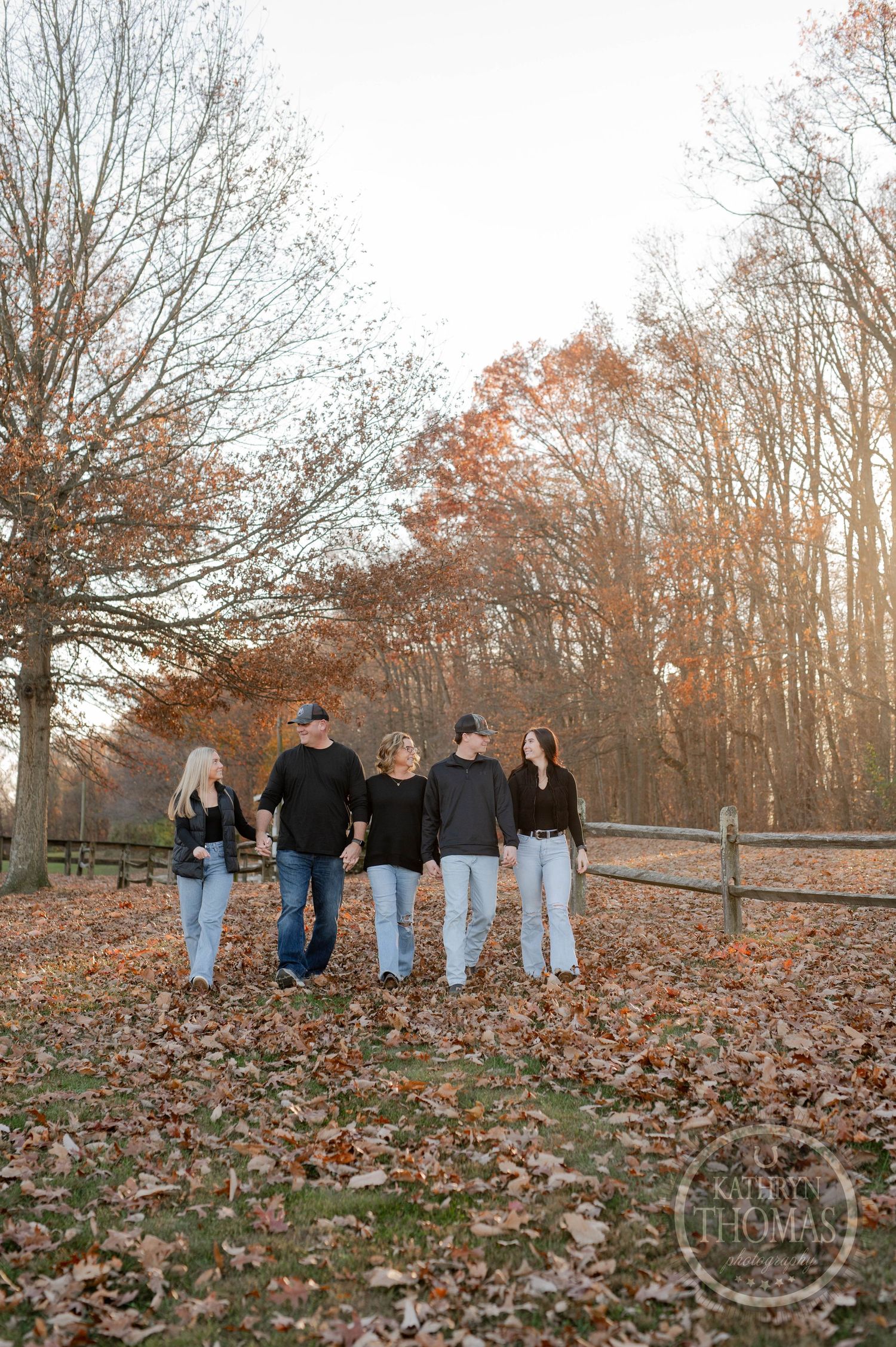Group walking together on fallen leaves by rustic split-rail fence in autumn forest.