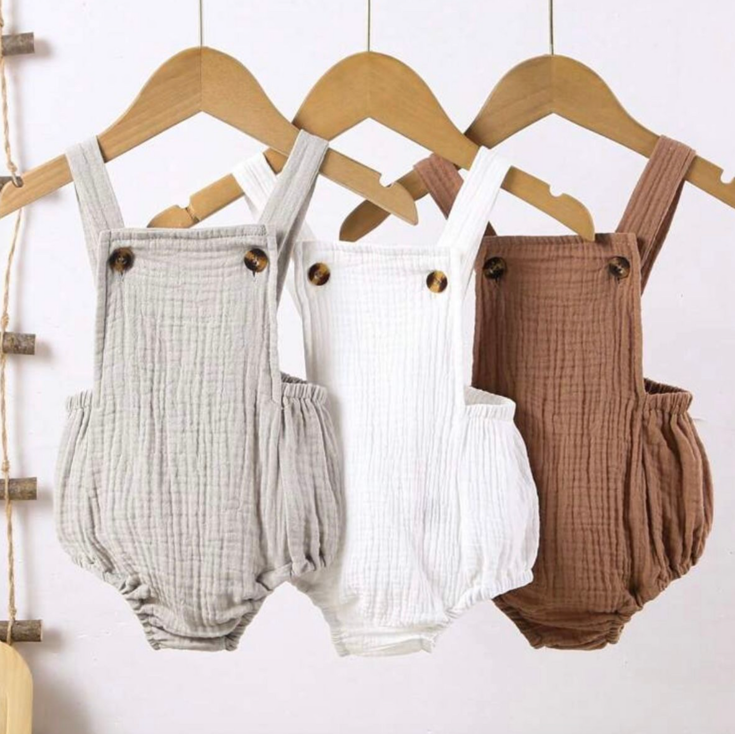 Collection of neutral colored muslin baby rompers hanging on wooden hangers.