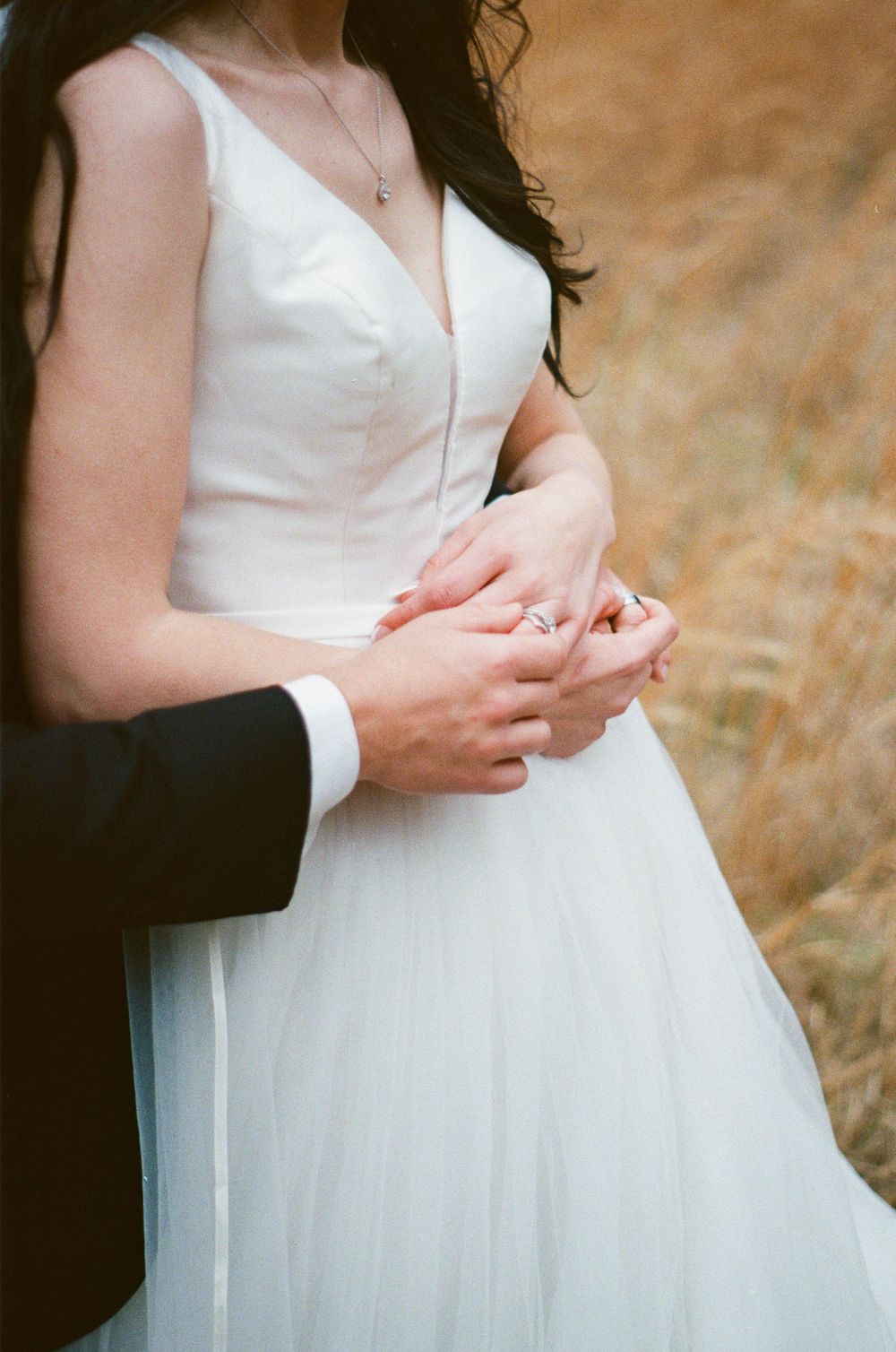 Closer shot of groom hugging bride from behind