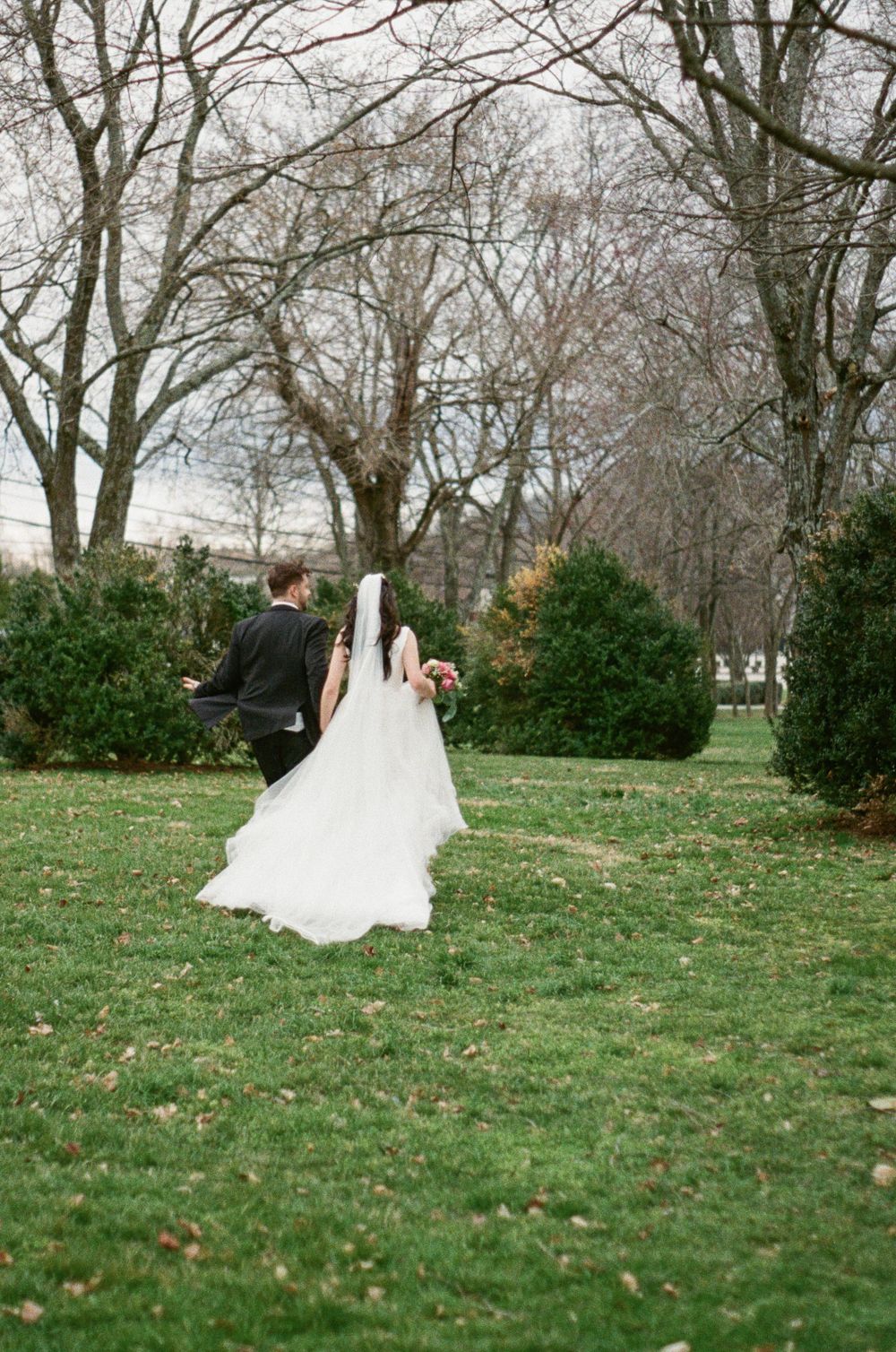 Bride and groom run through field towards trees