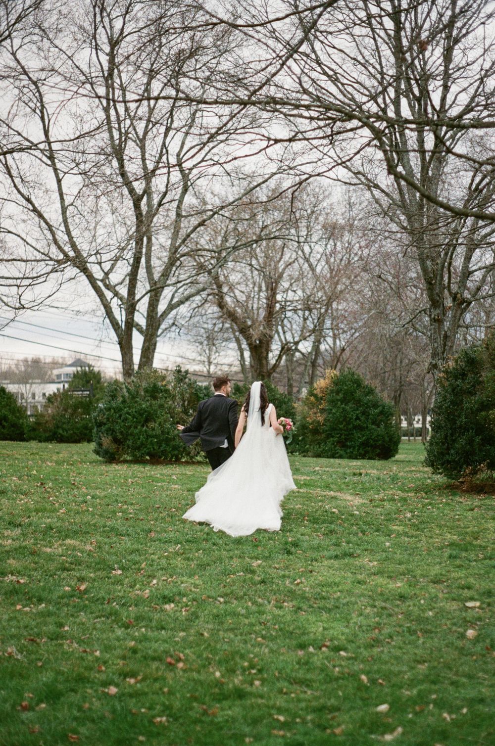 Bride and groom run through field towards trees