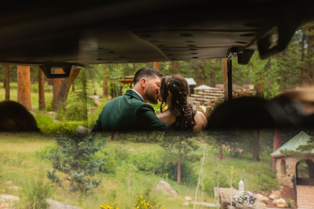 Romantic couple sharing intimate moment in nature reflected through car window during outdoor photoshoot.