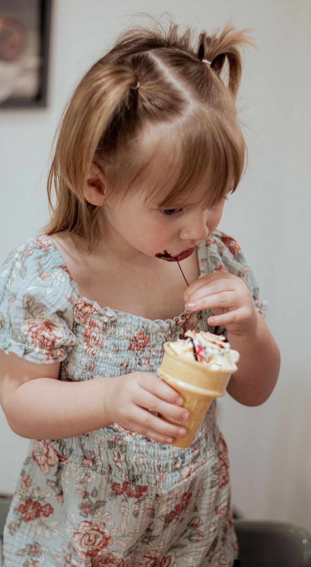 Little one in a floral dress enjoying an ice cream cone with visible delight.