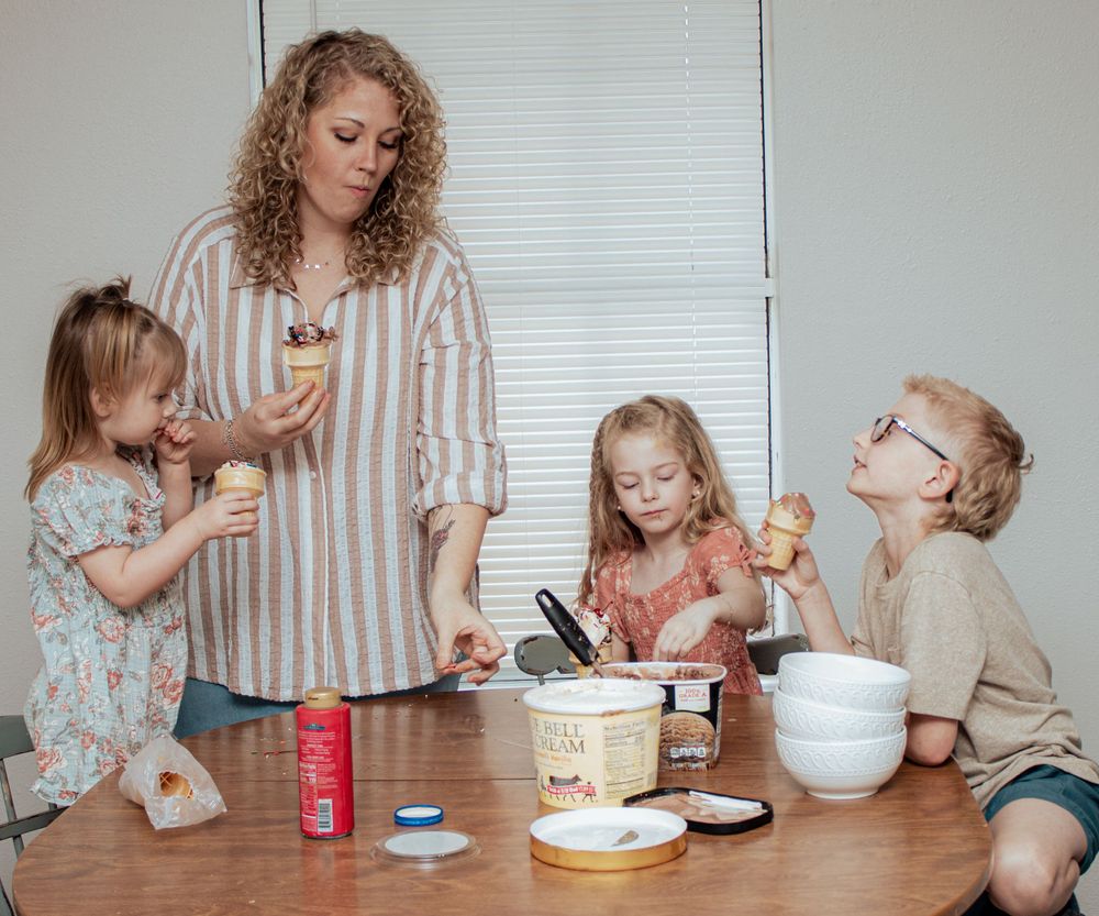 A group shares ice cream together at a wooden table with dessert toppings and containers.