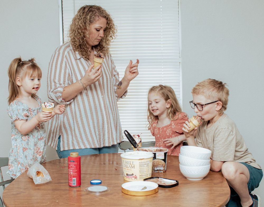 A group gathers around a table making dessert together with ingredients and mixing bowls spread out.