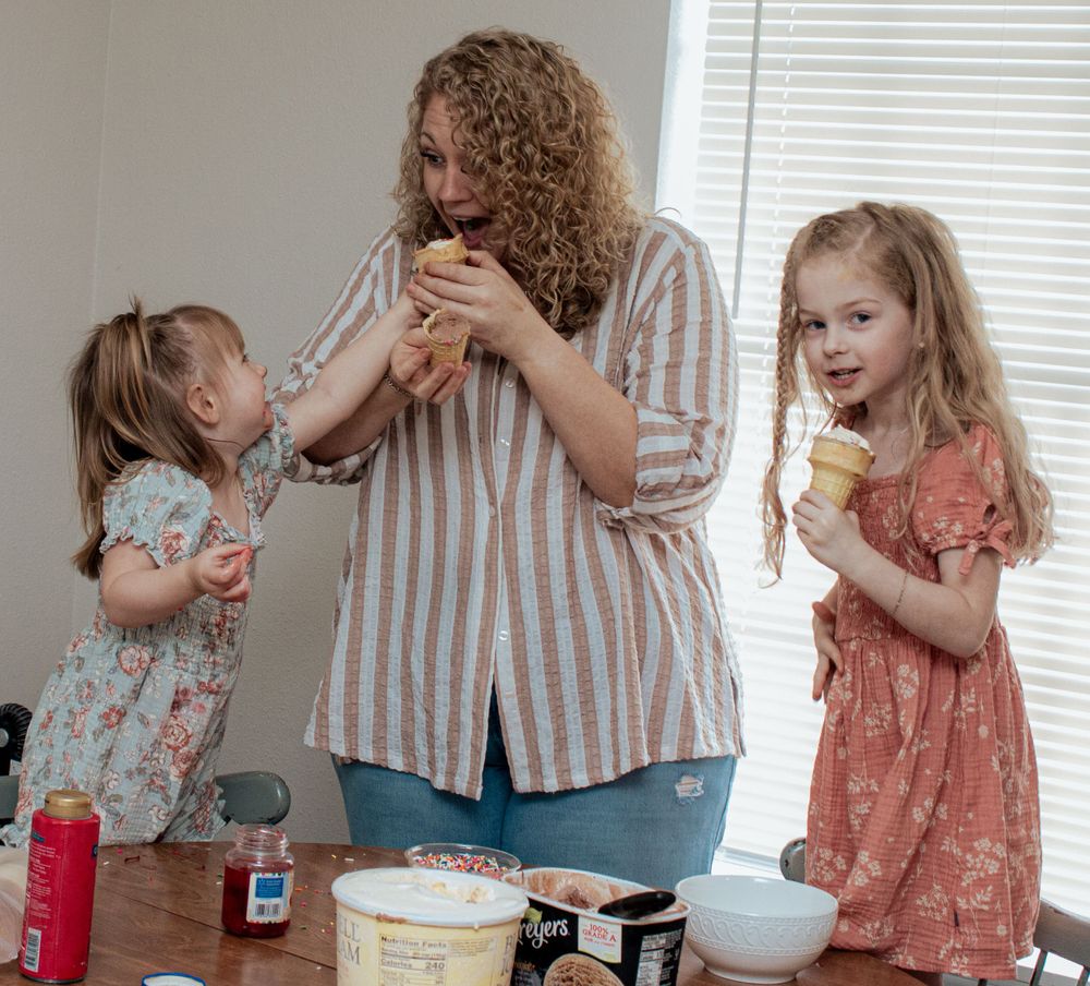 Several people gathered around a table enjoying ice cream treats during what appears to be a casual family moment.