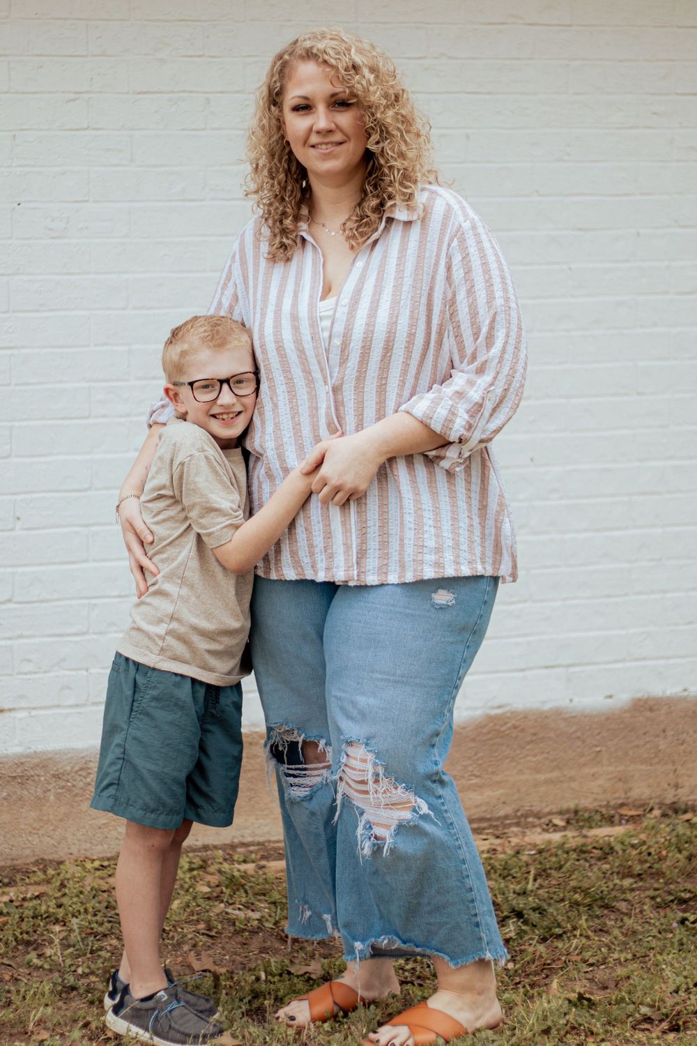 A family portrait outdoors showing casual affection and hugging against a white brick wall.