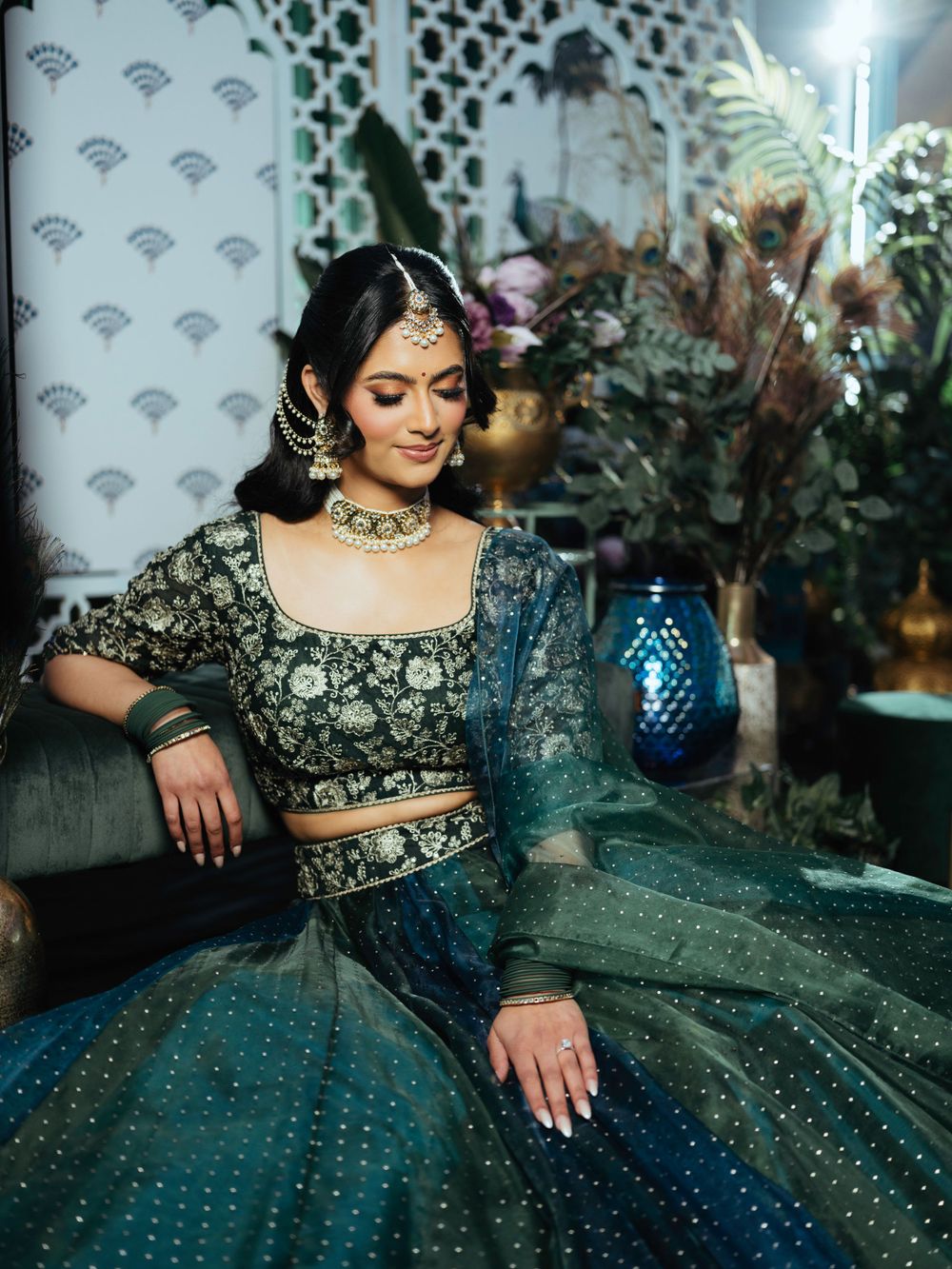 An elegant traditional Indian lehenga in teal and gold with intricate embroidery is paired with a blue glass lantern.