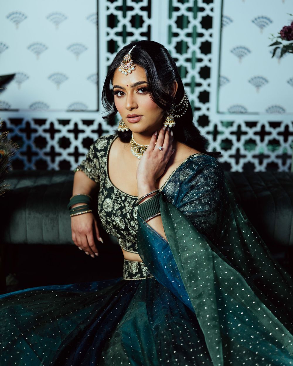 Traditional Indian-inspired formal attire in deep teal sparkles against decorative white latticework backdrop.