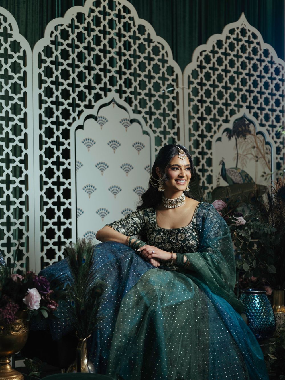 Traditional Indian wedding attire featuring an ornate teal and blue sequined lehenga against a decorative lattice backdrop.