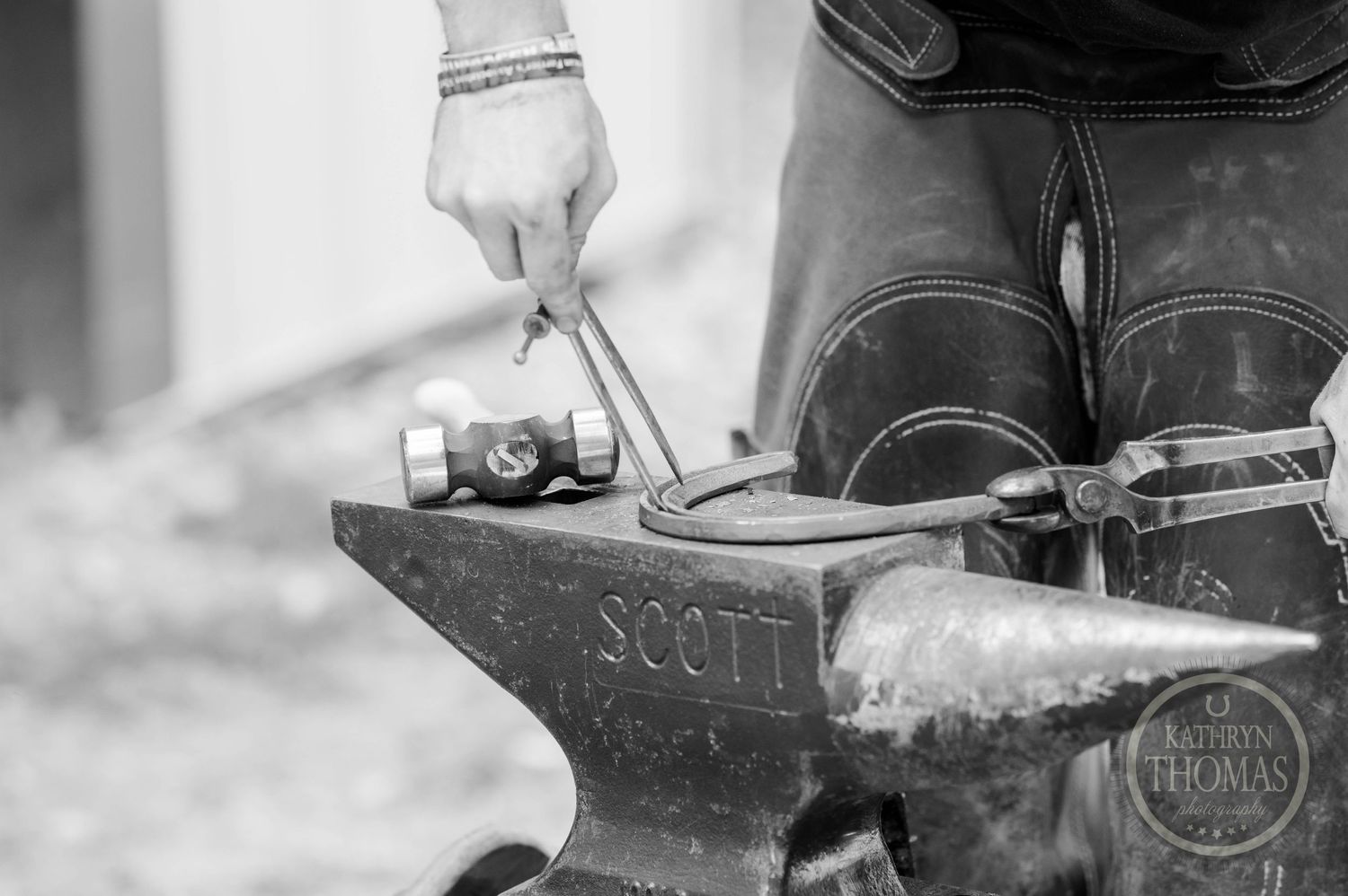 Black and white detail of tools and hands working on a Scott anvil.