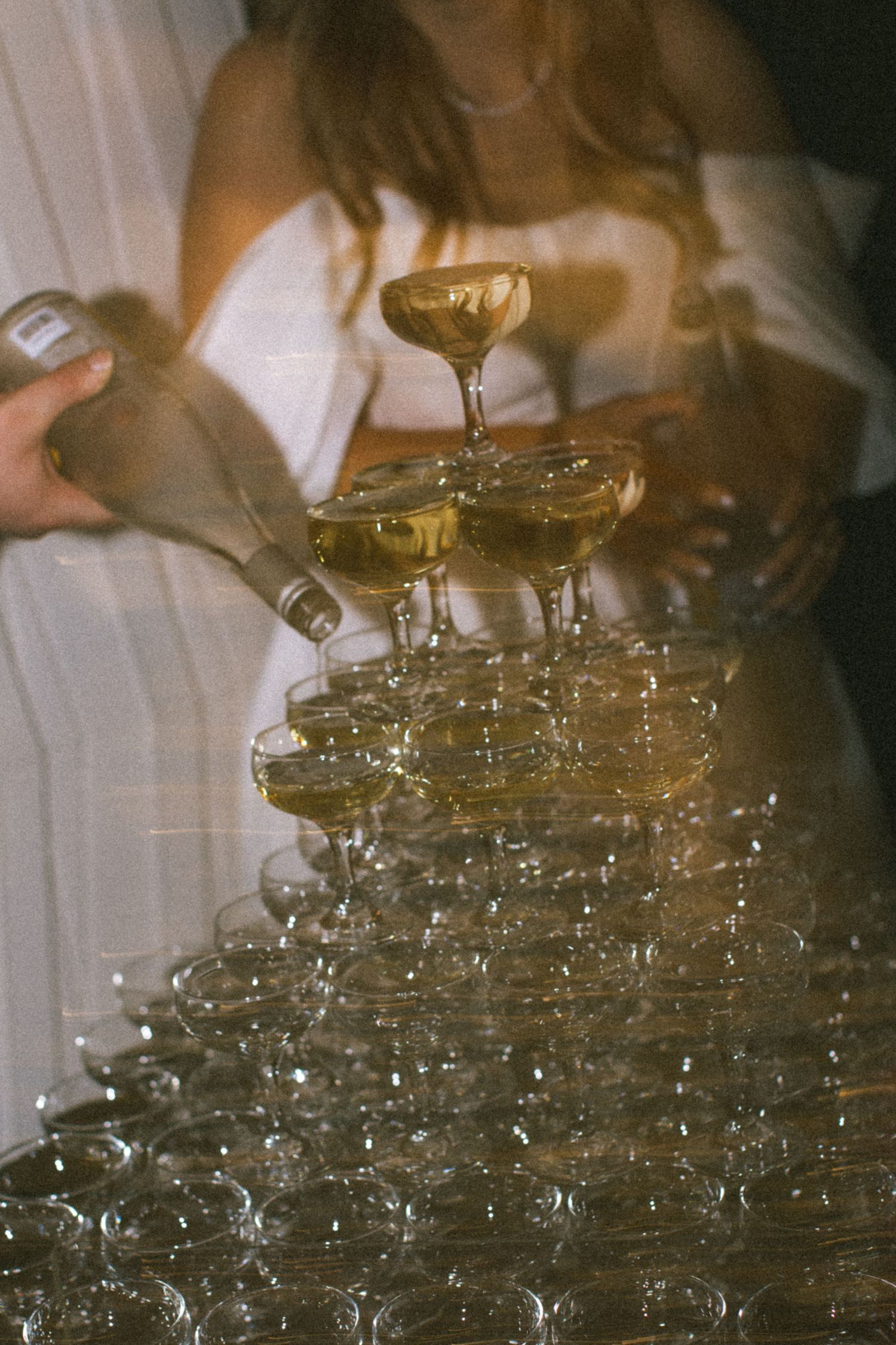 A bottle of Veuve Clicquot champagne with blue floral design lies beside pink roses and a crystal glass on white fabric.