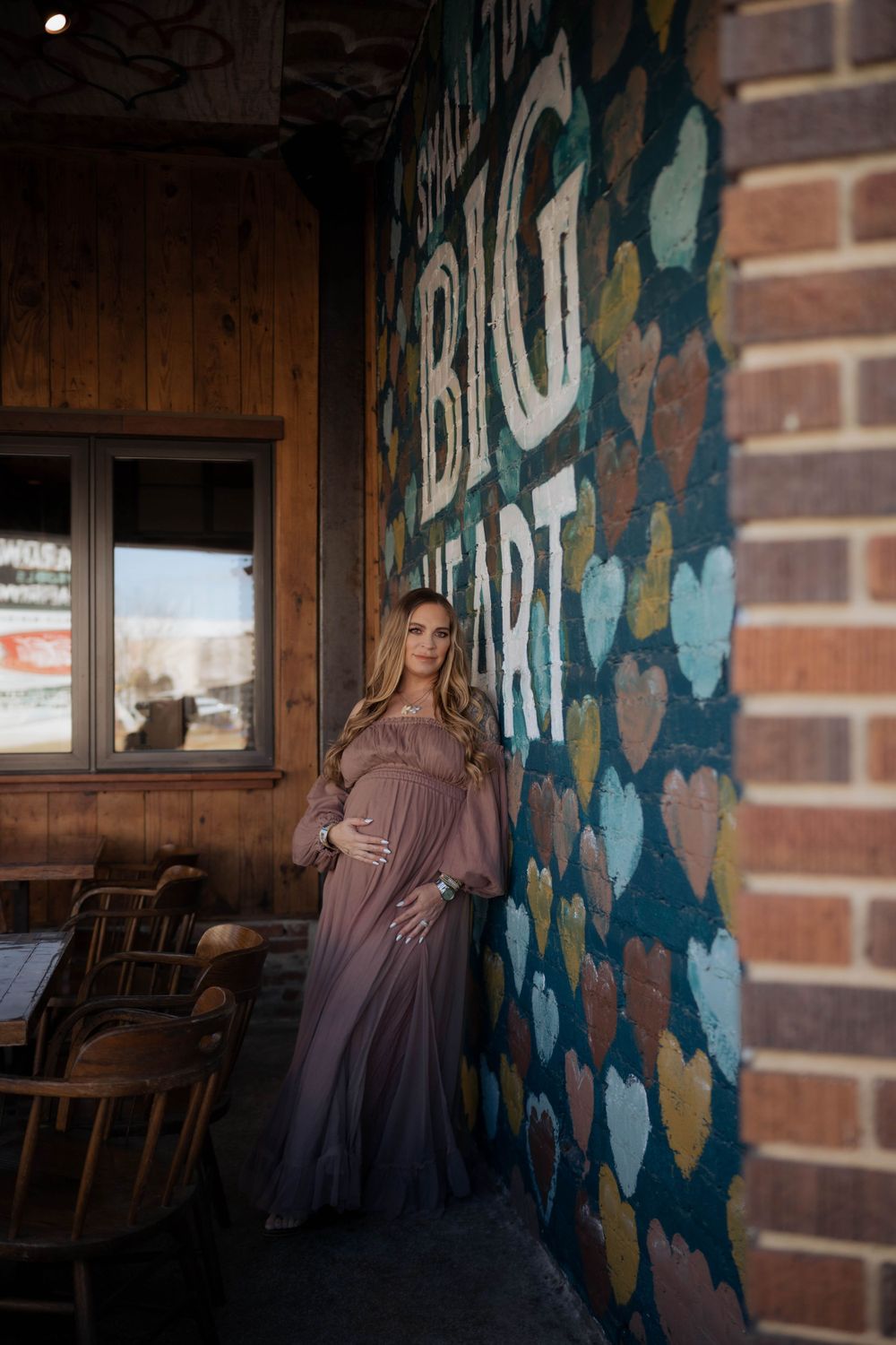 Elegant mauve dress stands against colorful heart mural on brick wall with wooden window frame in the background.