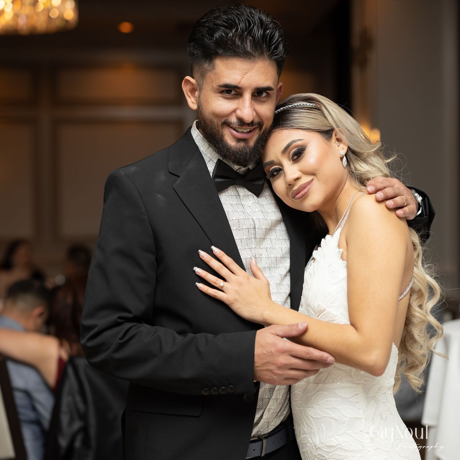 A romantic wedding couple embraces during their reception, with the bride in white and groom in black tie.