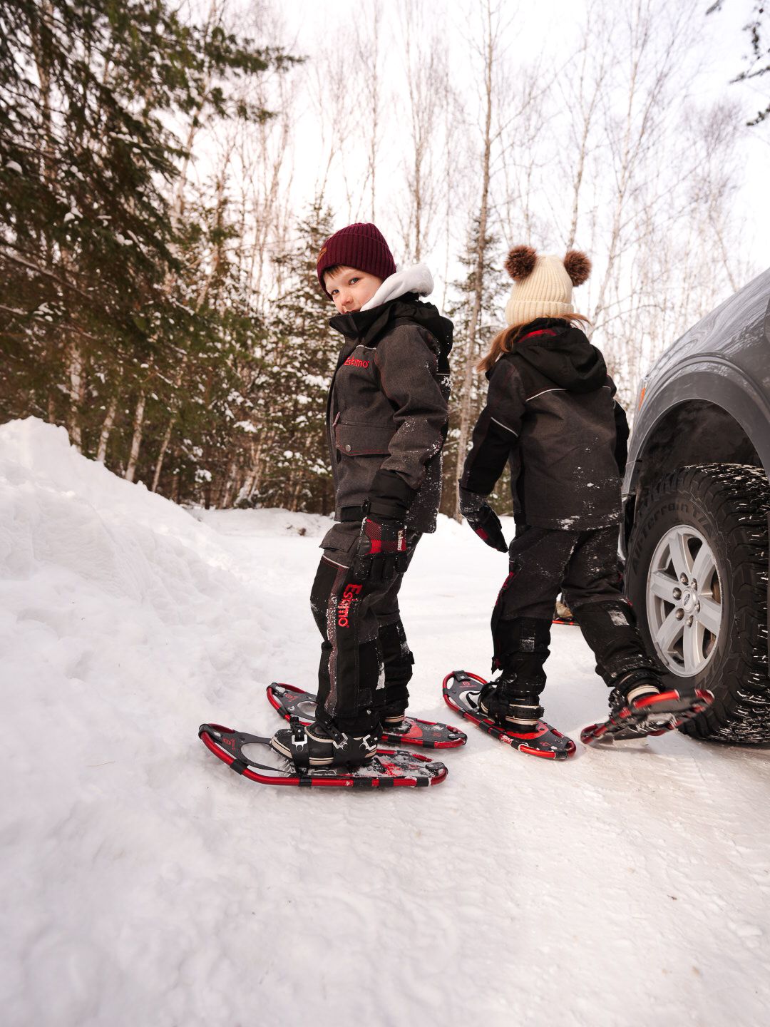 People kneeling in the snow while wearing snowshoes near a vehicle.
