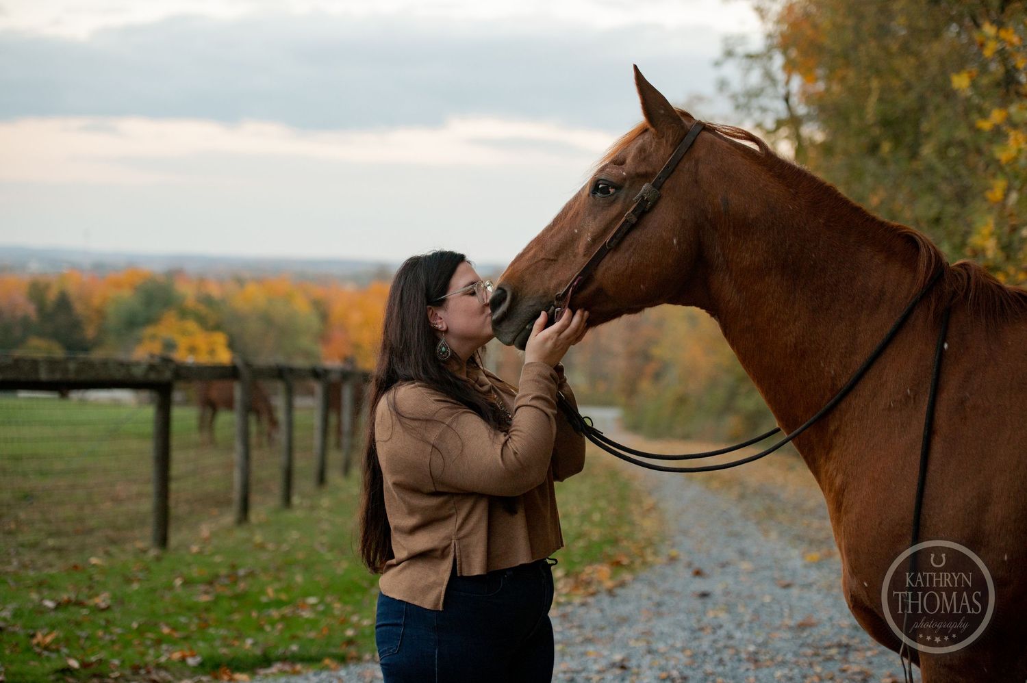 A tender moment between a person and their brown horse against an autumn landscape backdrop.