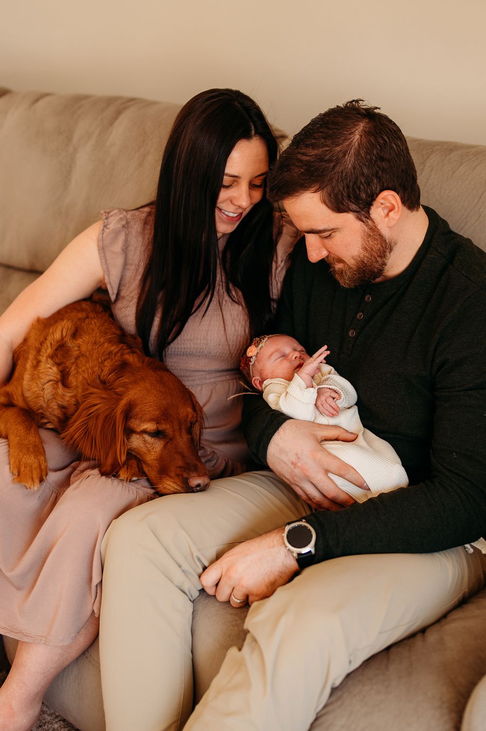 A family sits on a couch with their newborn baby and golden retriever dog.