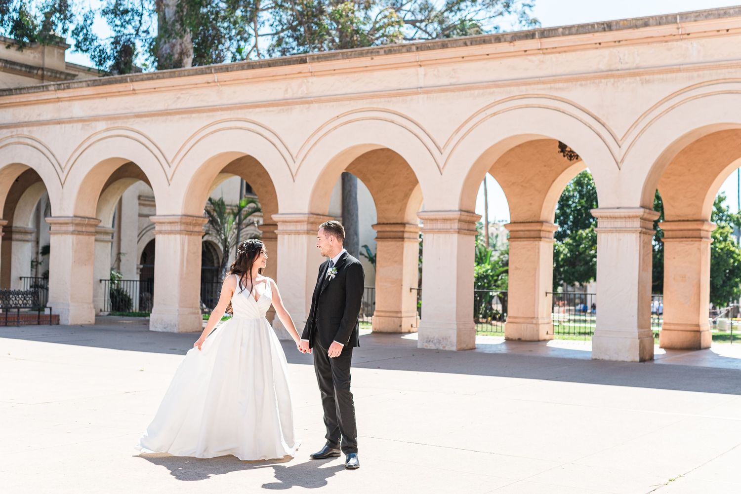 A couple in wedding attire standing under beautiful arched columns at a historic venue.