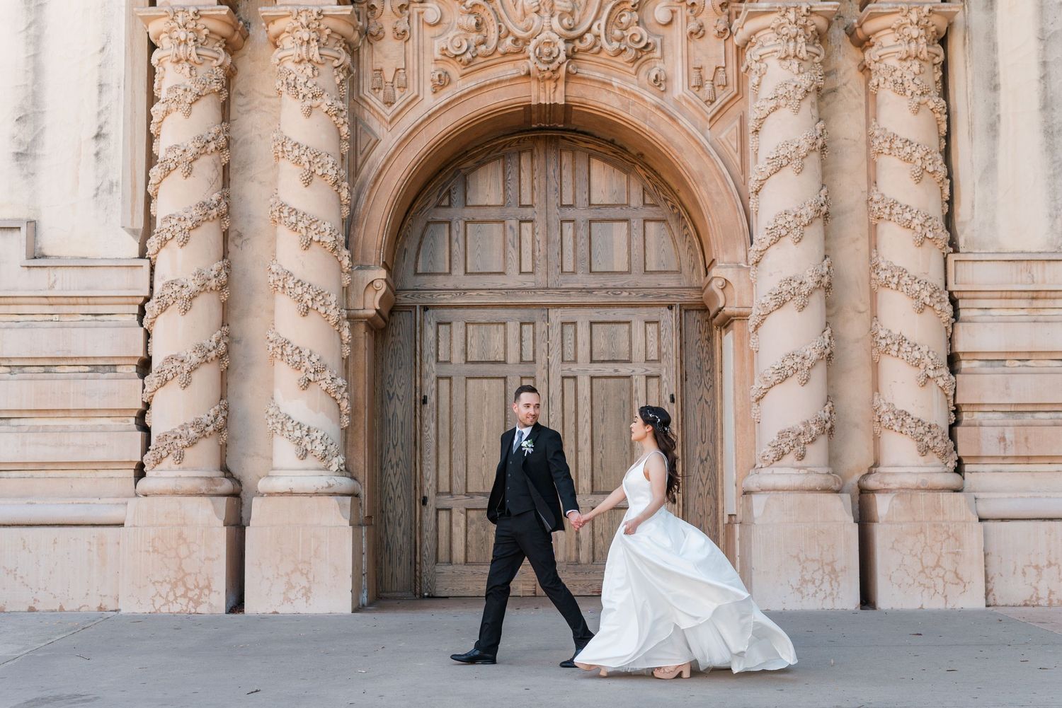A couple posing in front of an ornate architectural doorway with detailed stone carvings.