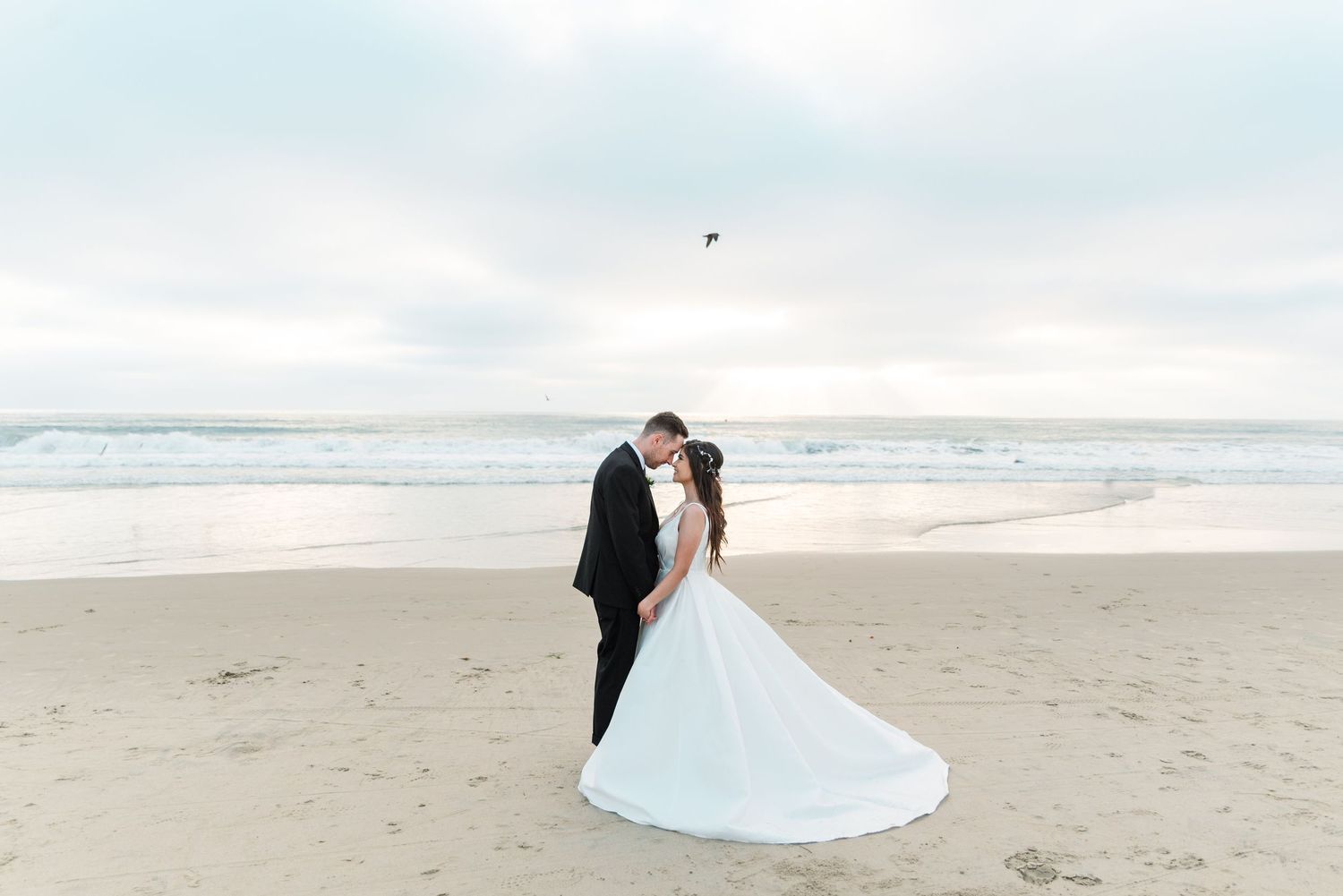 A couple in wedding attire standing together on a misty beach at sunset.