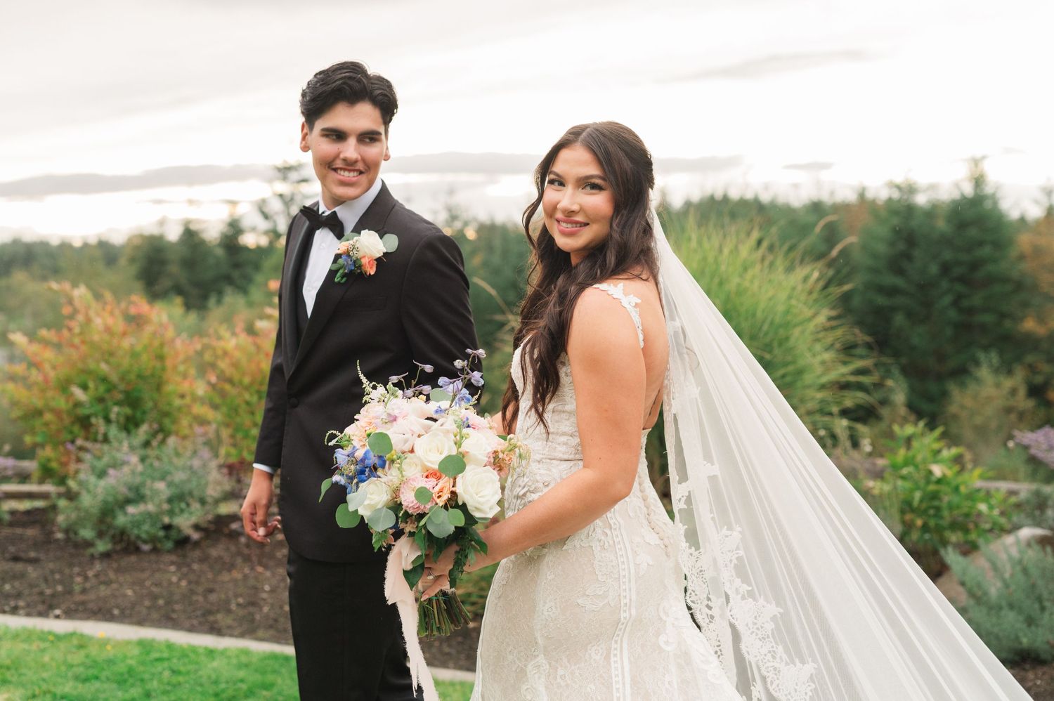 A couple posing together outdoors with a floral bouquet against a natural landscape.