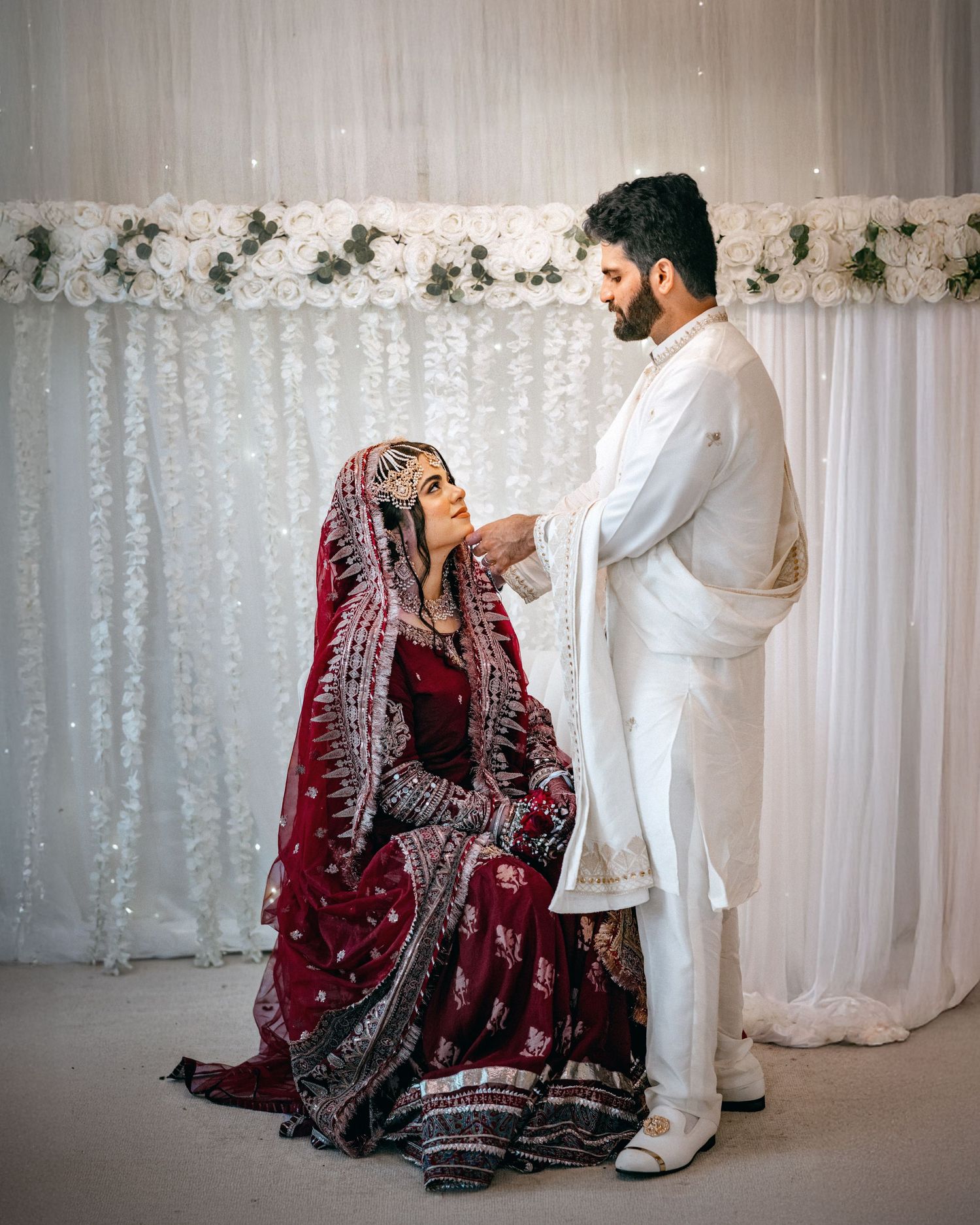 Traditional South Asian wedding ceremony with elegant decor featuring white curtains and floral arrangements.
