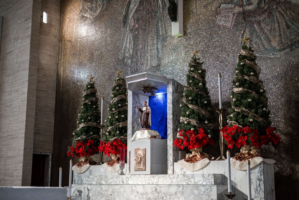 Church altar decorated with Christmas trees, poinsettias and a crucifix with religious artwork in the background.