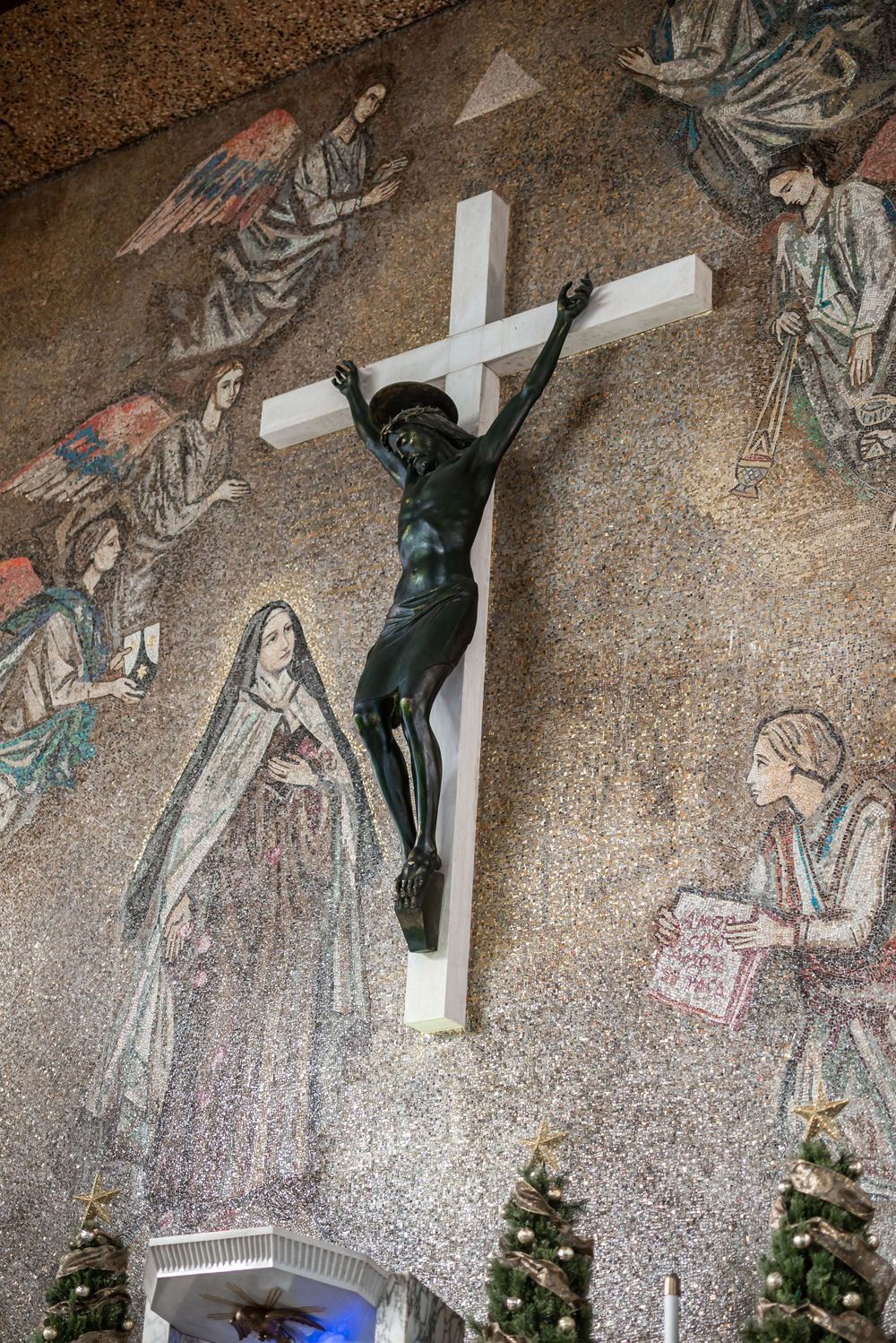 A large crucifix mounted on a wall with angel murals and Christmas trees below.