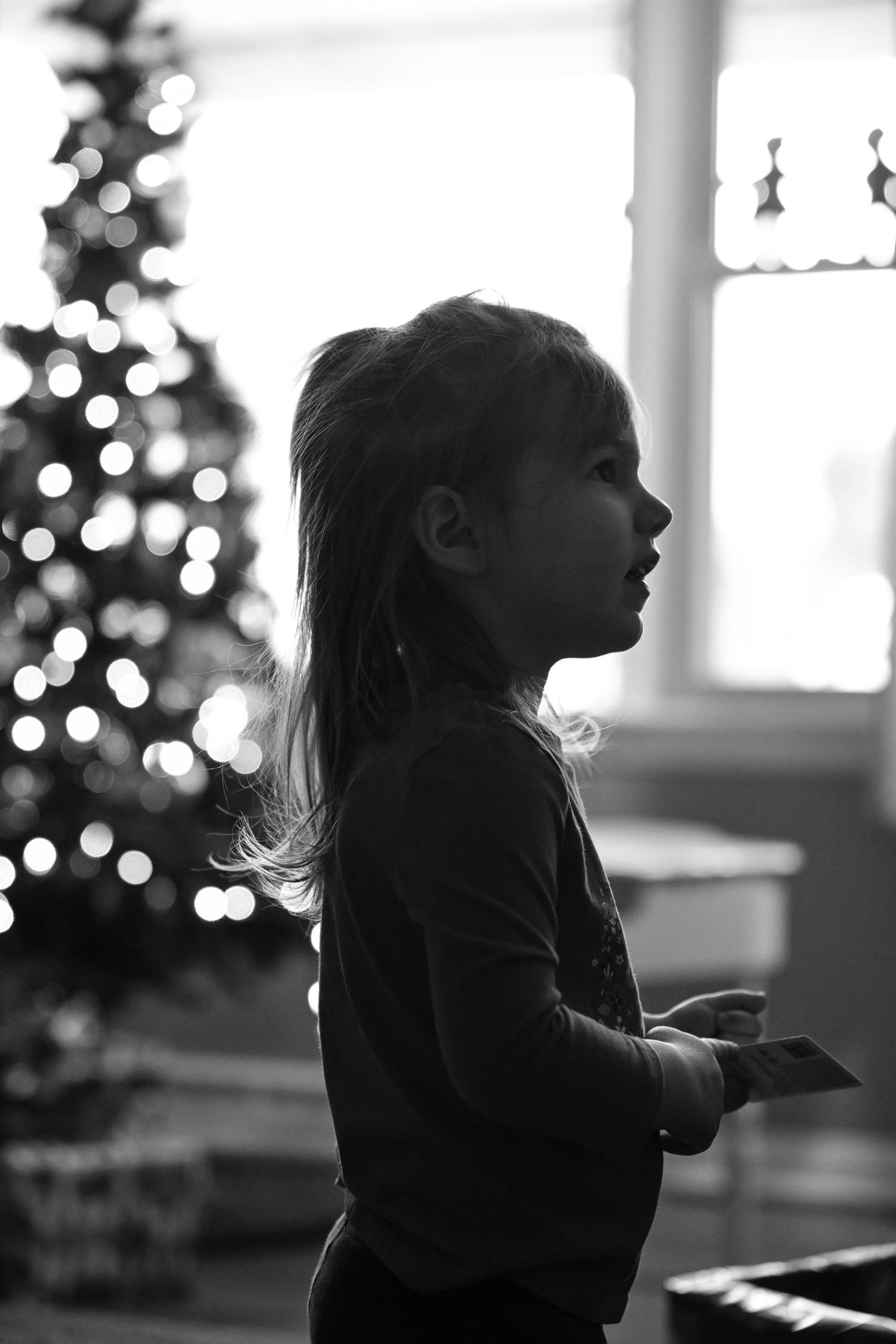 A black and white image of Emma standing in the living room, backlit by the windows behind her
