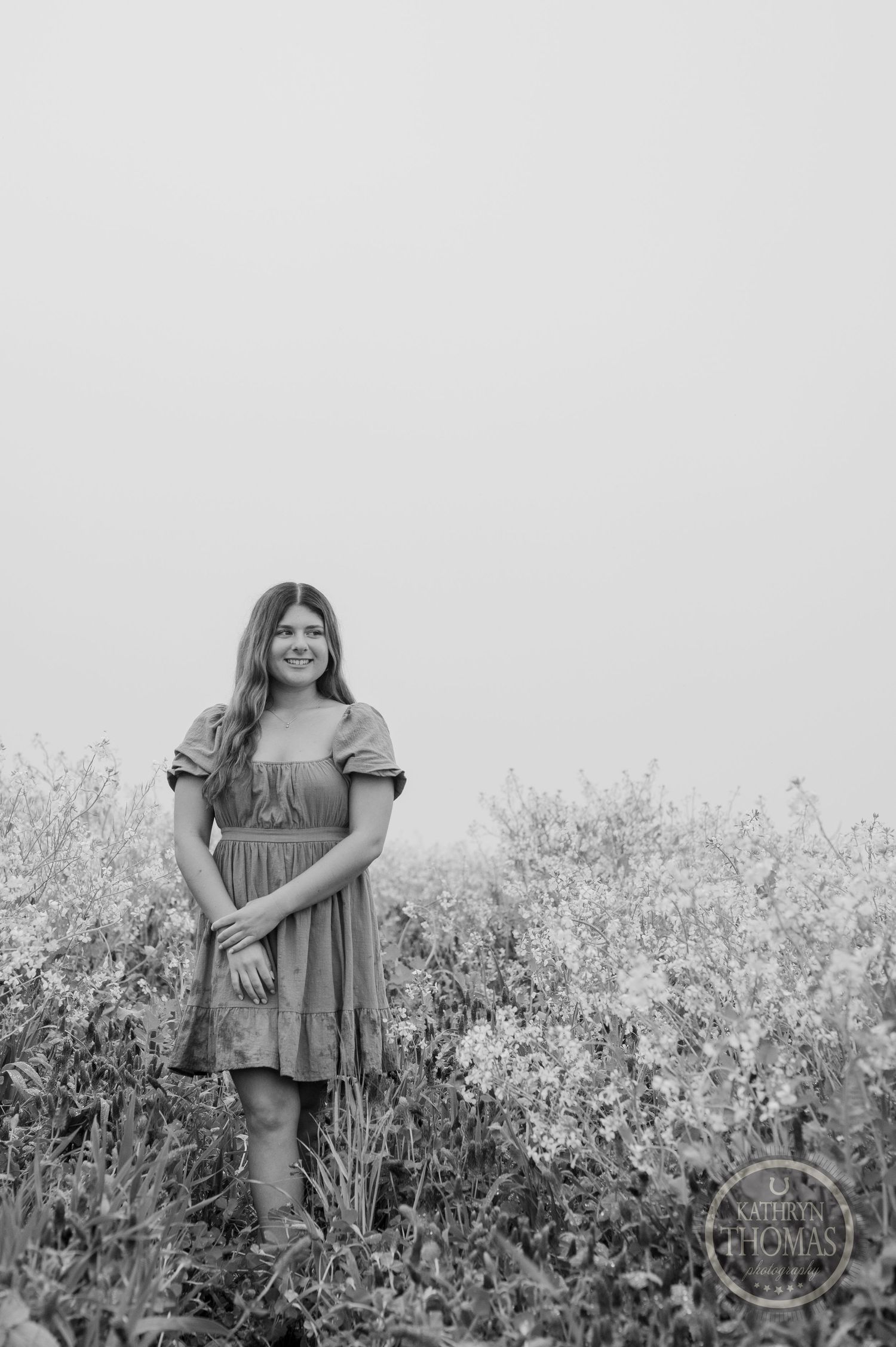 A black and white portrait of someone in a prairie dress standing in a field of wildflowers.
