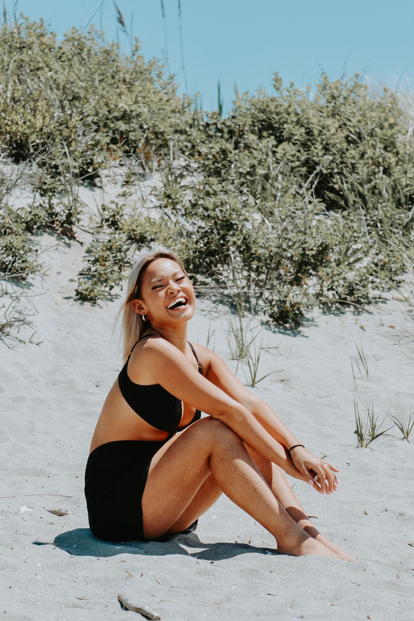 Summer beach portrait of person sitting on sand wearing black swimwear.