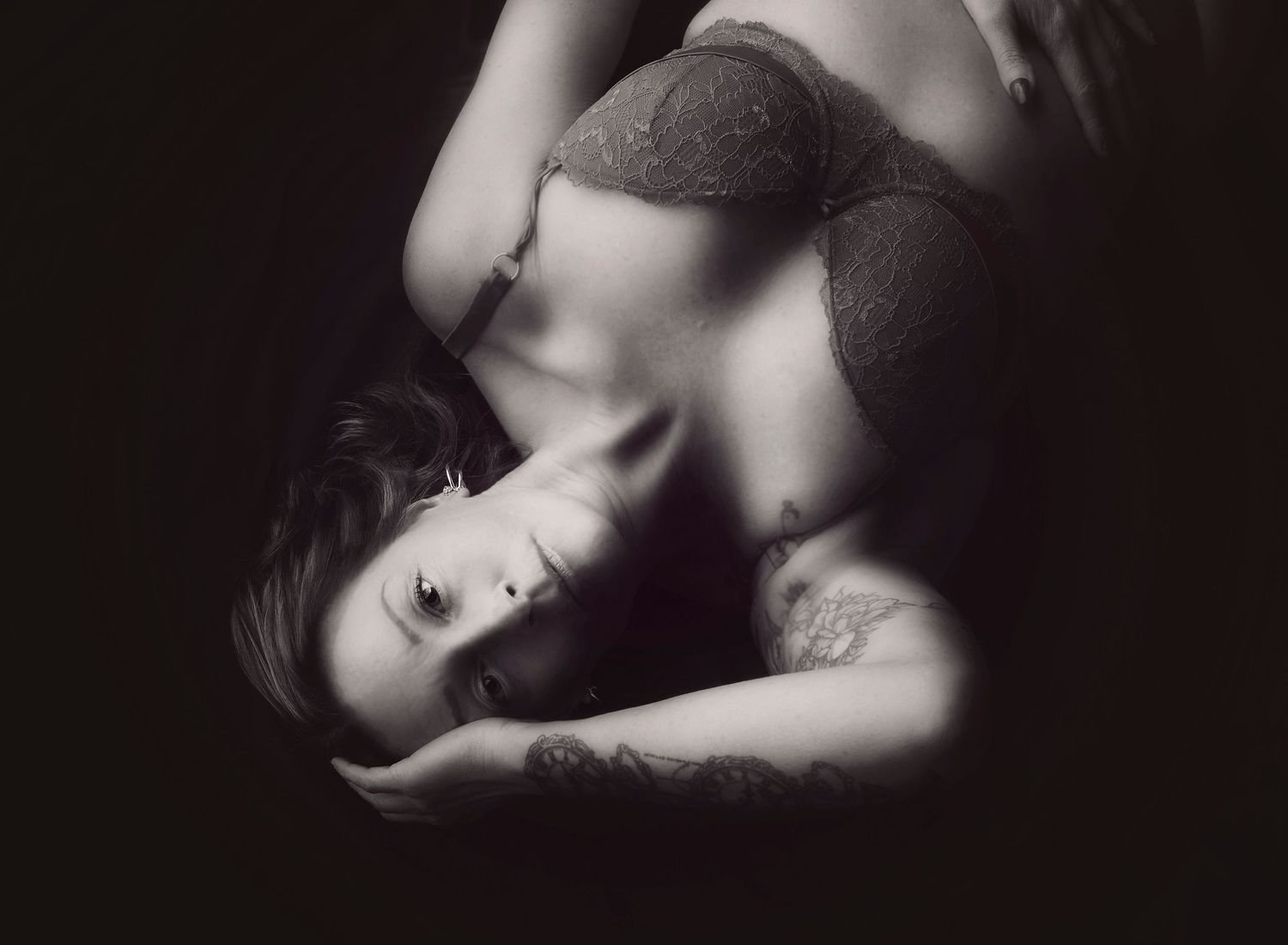 Black and white boudoir image, lying on the floor, hand in the hair, looking directly at the camera, eludes confidence.