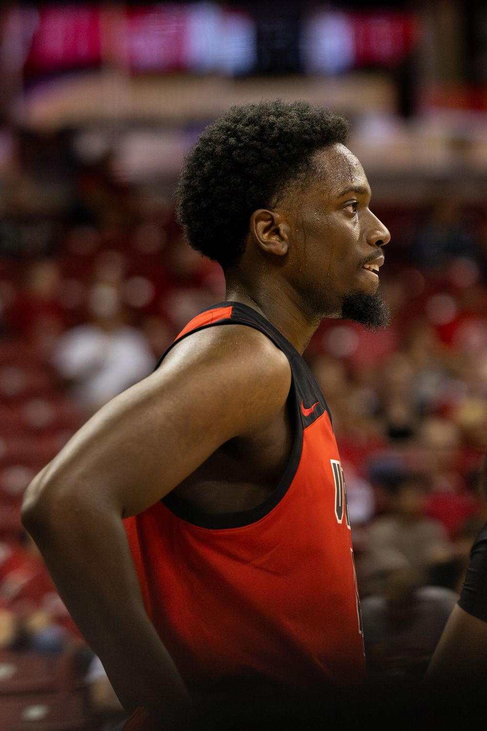 Basketball player in red jersey looking on from sideline during game.