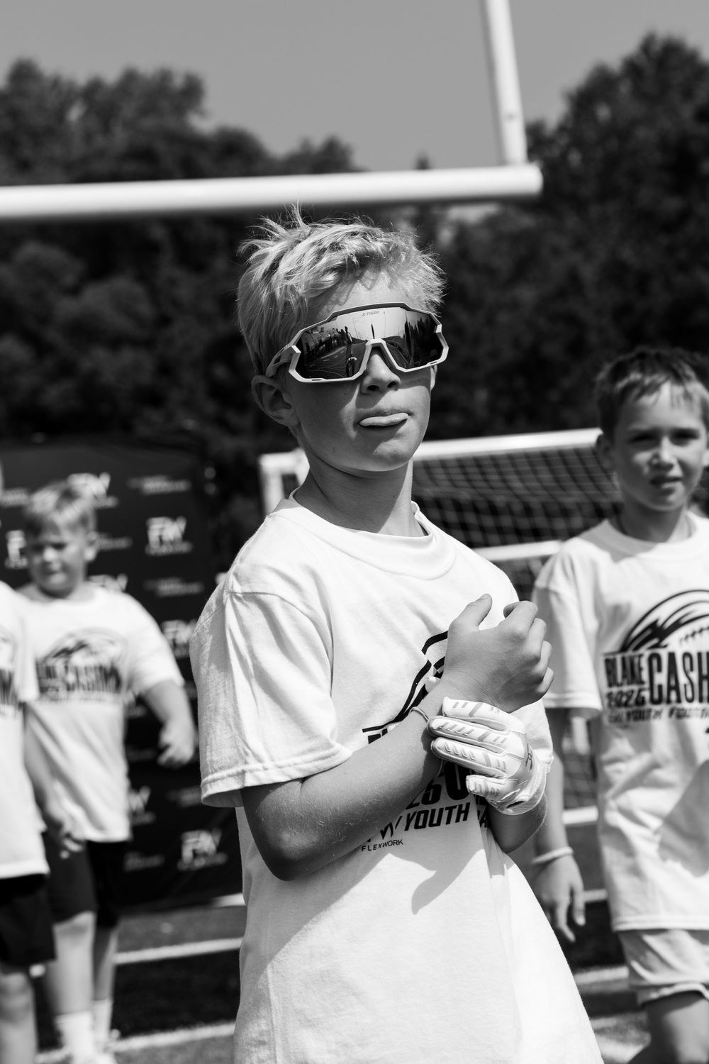 Young athlete in sunglasses and white t-shirt at outdoor sporting event on sunny day in black and white photo.