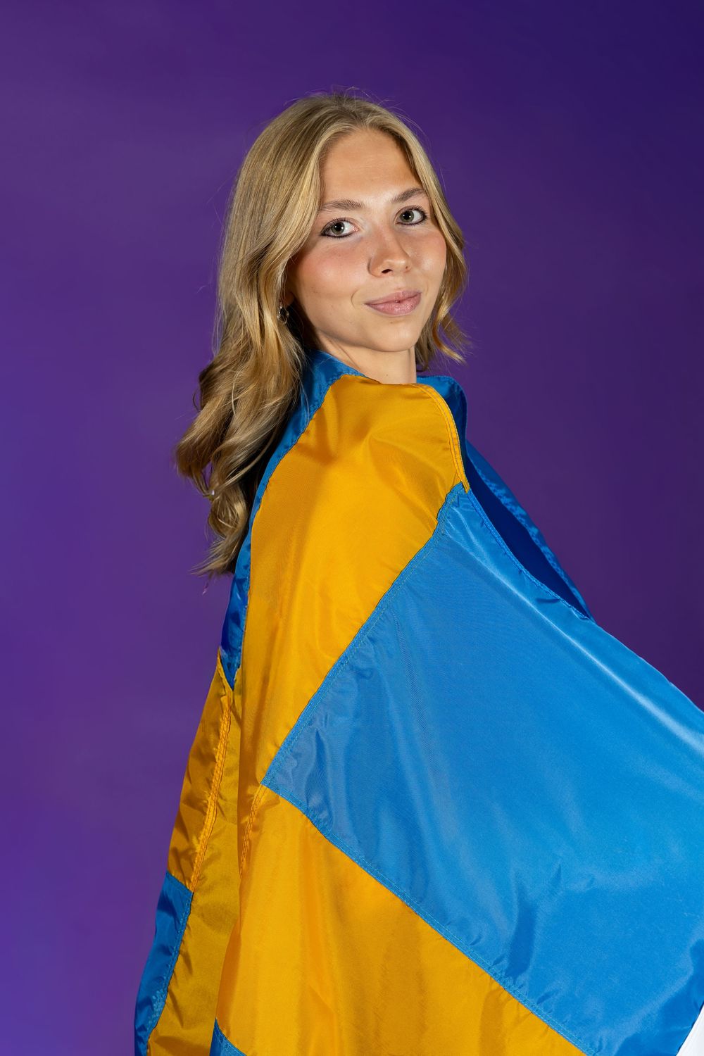 Person in bright yellow and blue color block outfit poses playfully against purple background.