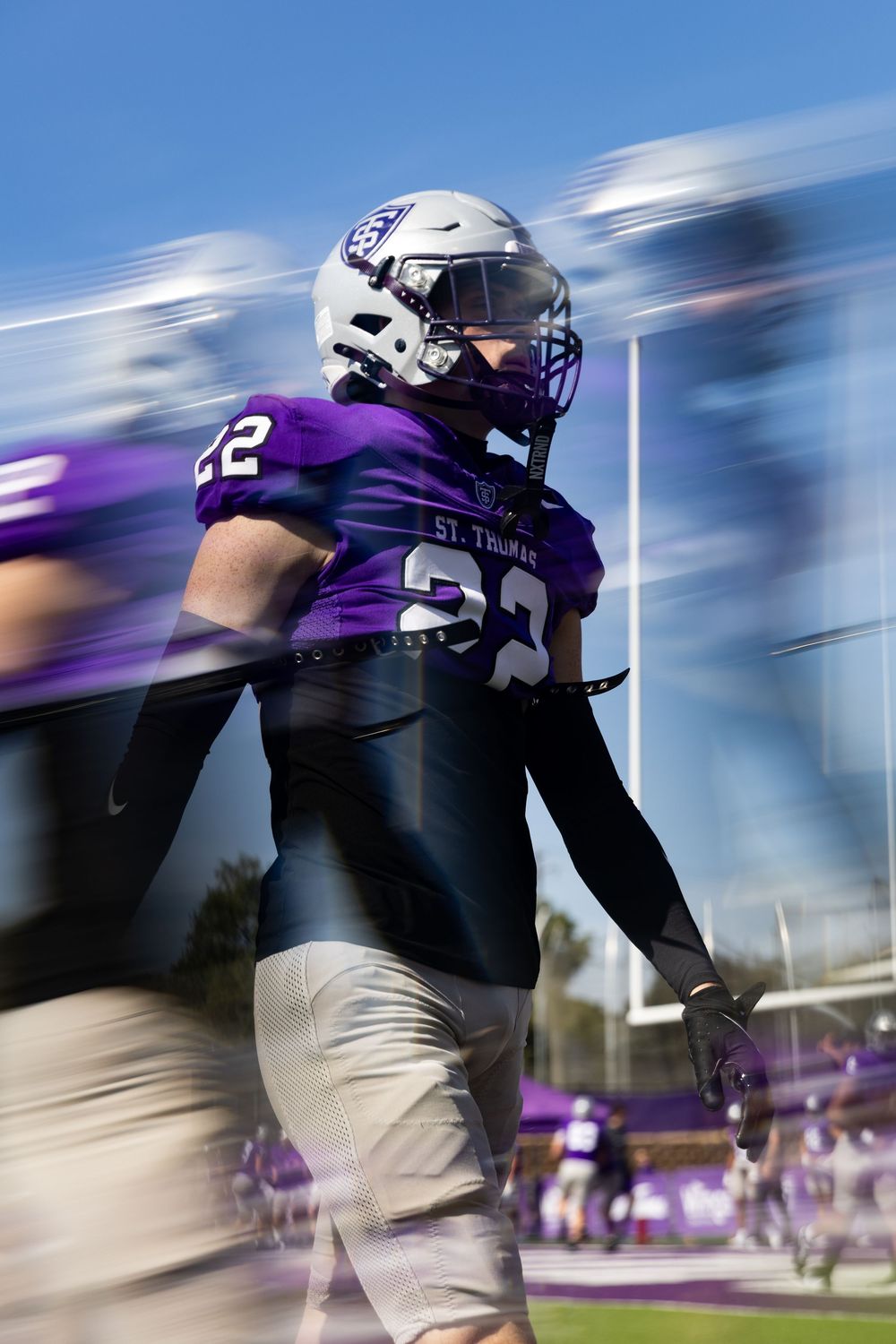 Motion blur effect shows football players in purple jerseys running across field during game action.