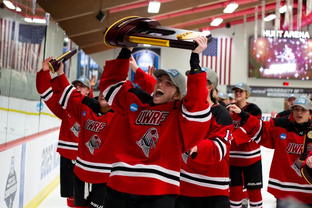 Hockey players in red jerseys celebrating on the ice with raised sticks.