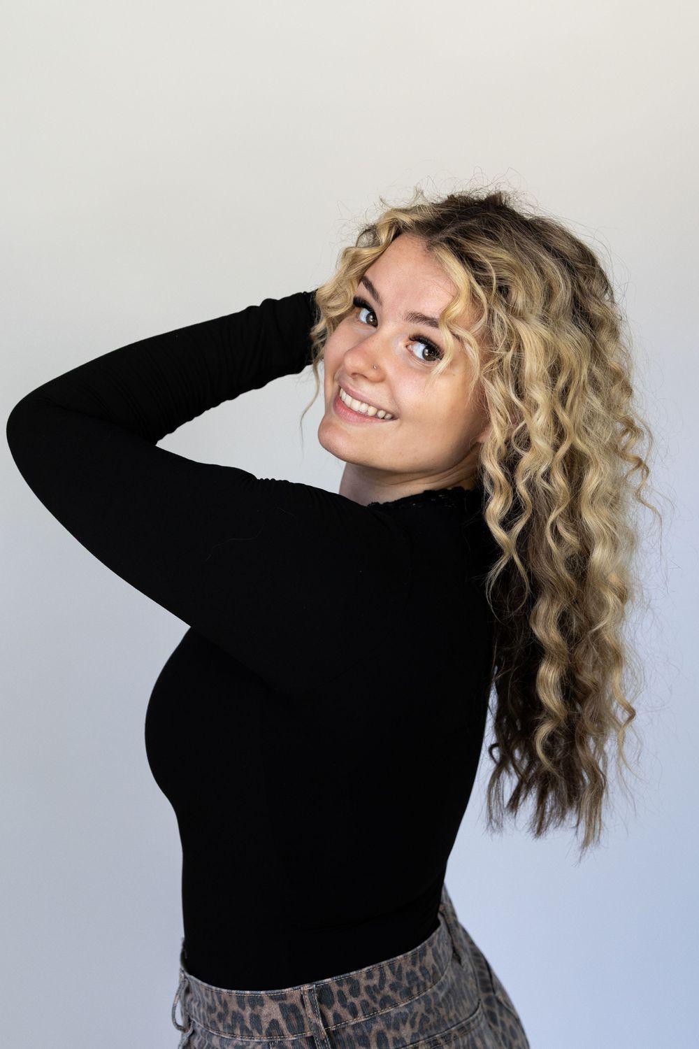 Person with curly blonde hair wearing a black sweater poses playfully against light blue background in four different shots.