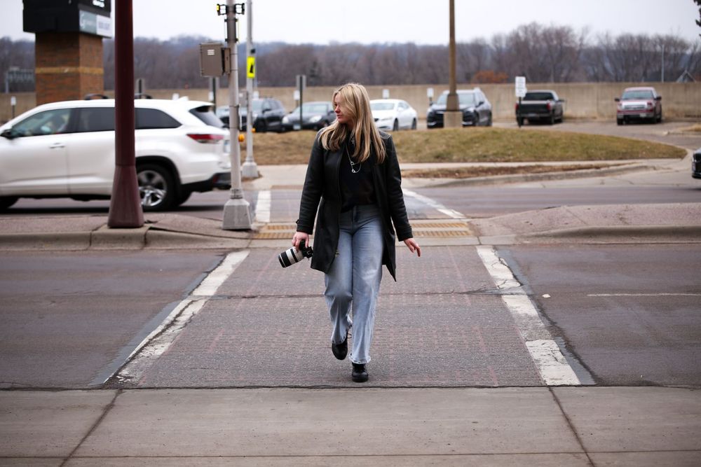 Person walking across crosswalk carrying camera in winter urban setting.