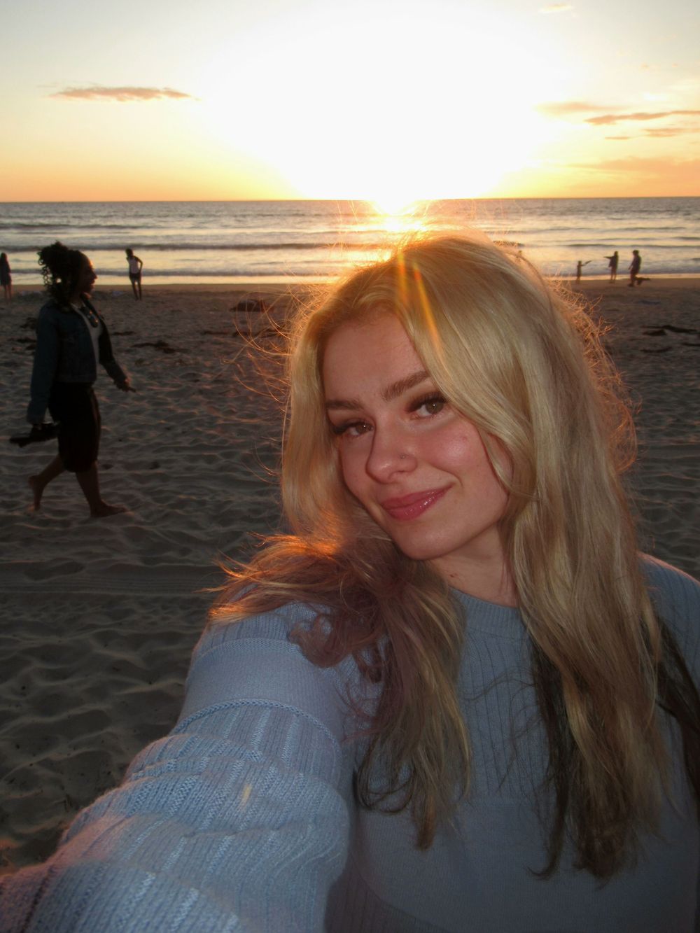 Beach sunset selfie with golden light illuminating long blonde hair against an ocean backdrop.