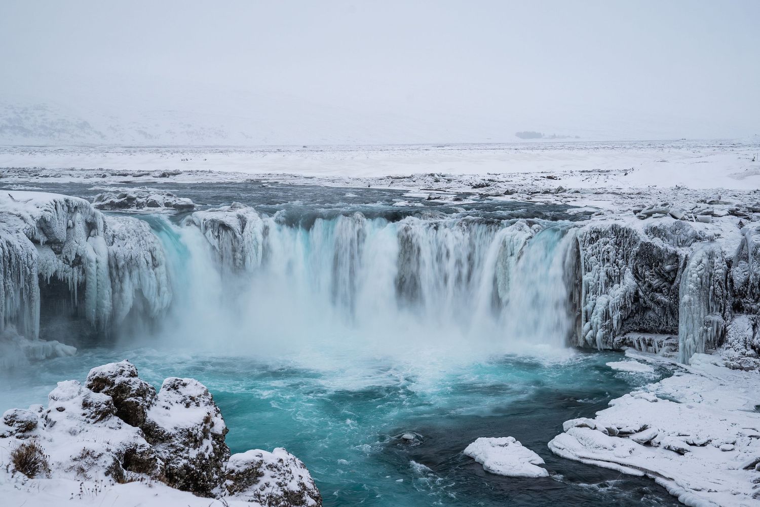Godafoss waterfall in Iceland cascades over icy cliffs into turquoise waters during winter.